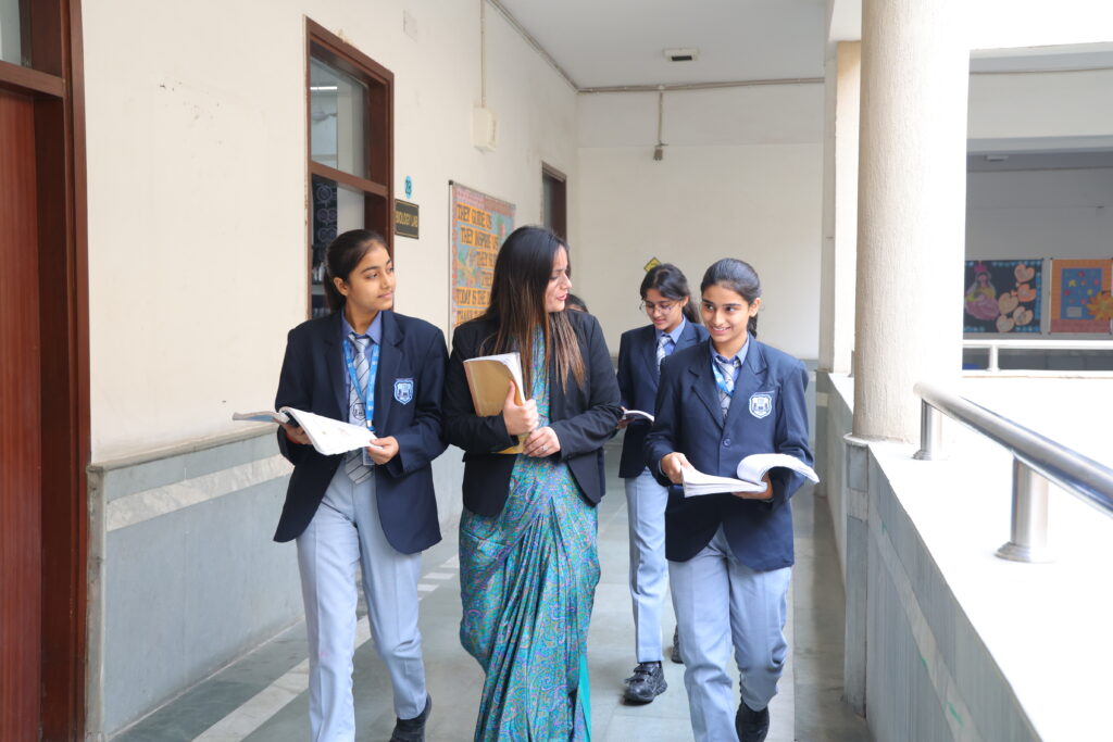 Teacher and students walk and converse in a school corridor with books in hand