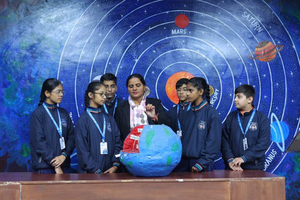 Students and teacher explore a large globe with a space-themed mural backdrop